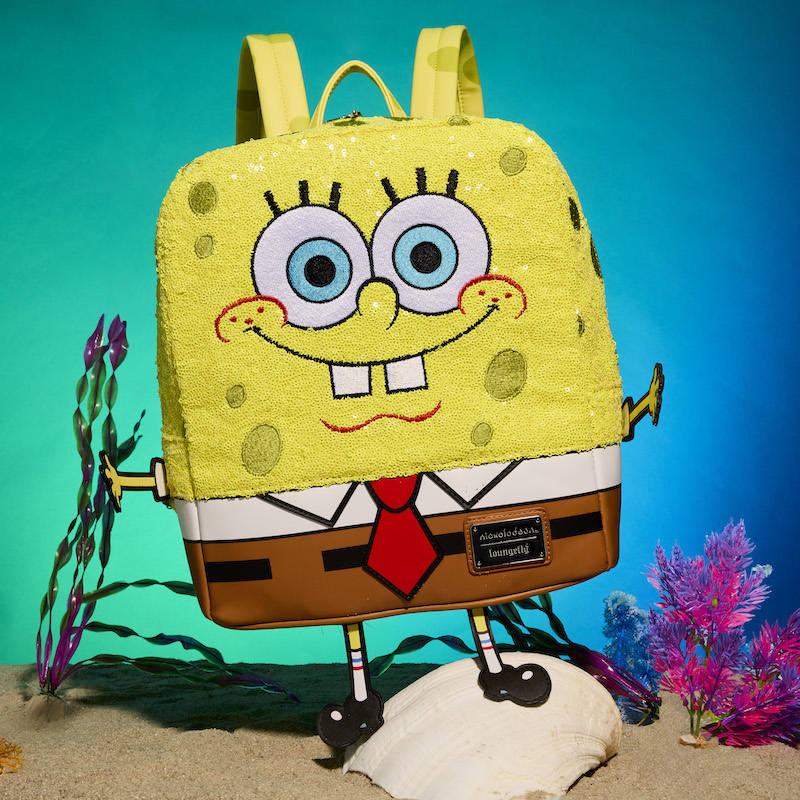 Loungefly Exclusive Sequin SpongeBob SquarePants mini backpack standing on top of a shell in the sand, surrounded by aquatic plants and standing against a blue green ocean background. 